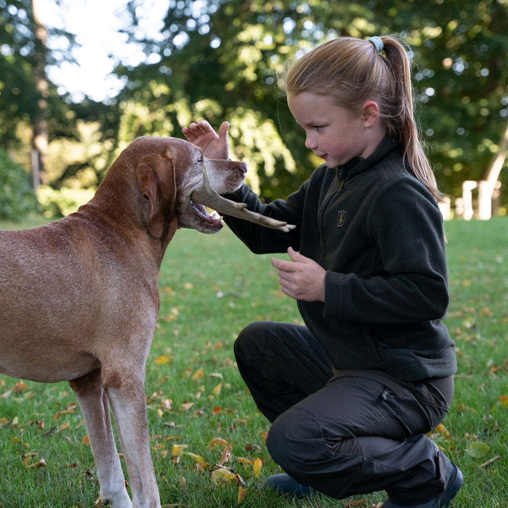 Kind in Deerhunter Youth Atlas Light Fleecejacke beim aktiven Spielen mit Hund auf einer Wiese